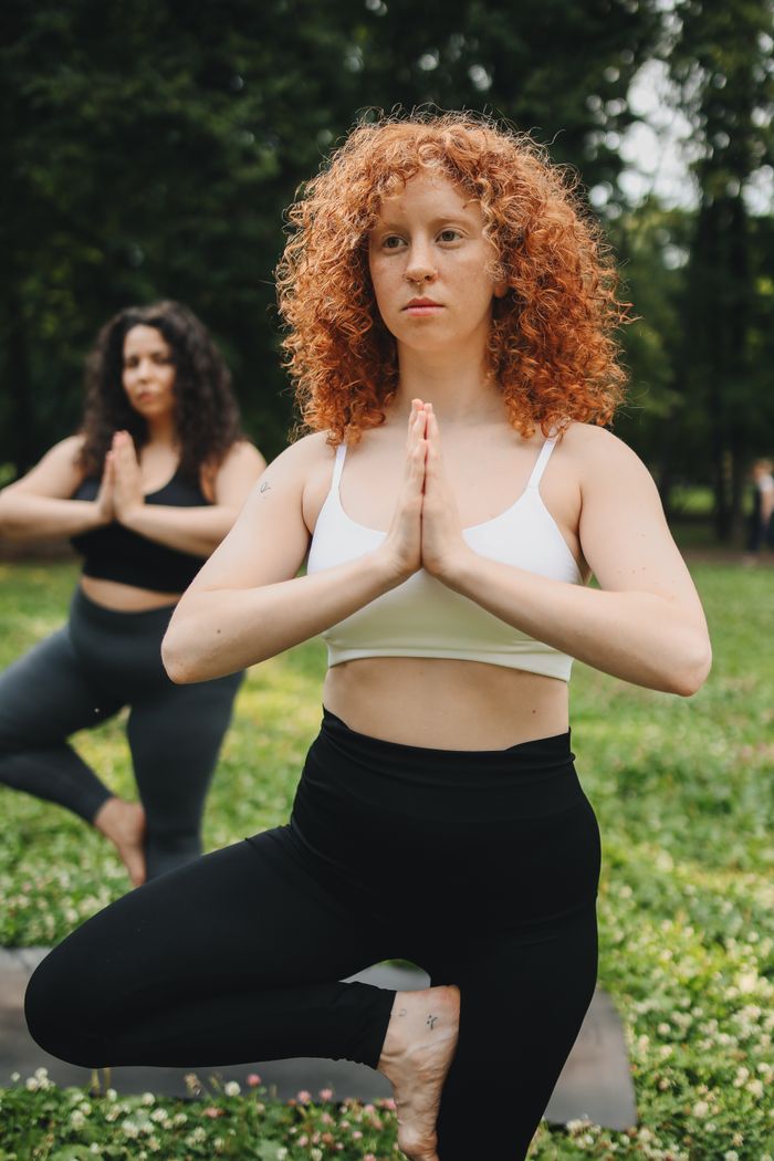 services-03 Two women practicing yoga poses in a lush outdoor setting, promoting wellness.
